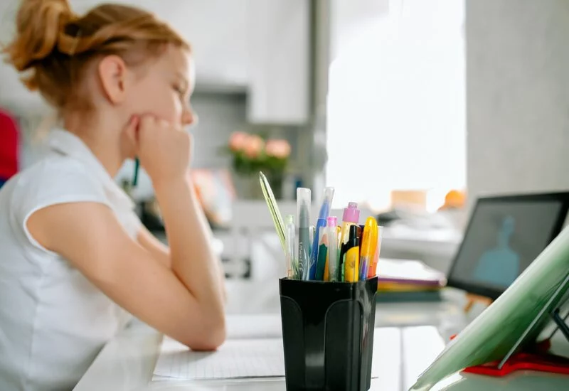 Child sat watching ipad on kitchen table with pens
