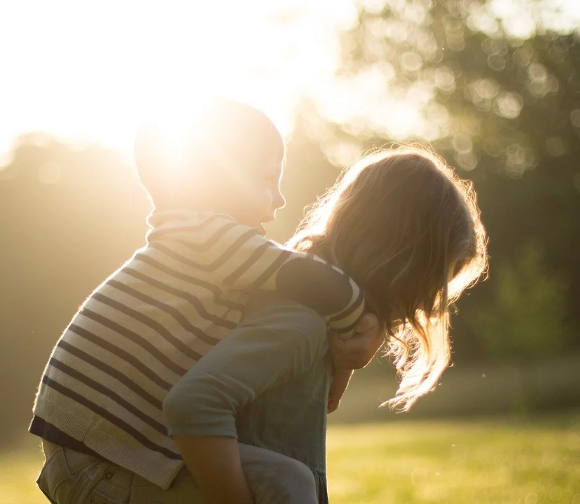 Brother and sister outside, giving piggyback to little brother in the sun