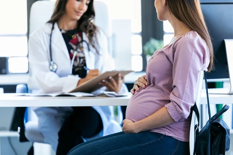 Pregnant women sat at with doctor going through questions a clipboard