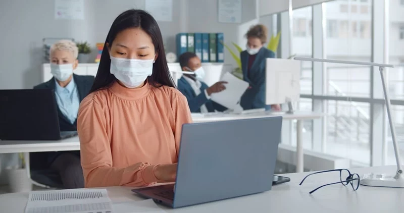 colleagues in the office with masks on and on laptops