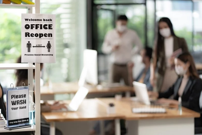 Welcome back office reopen sign and people in the background with masks on