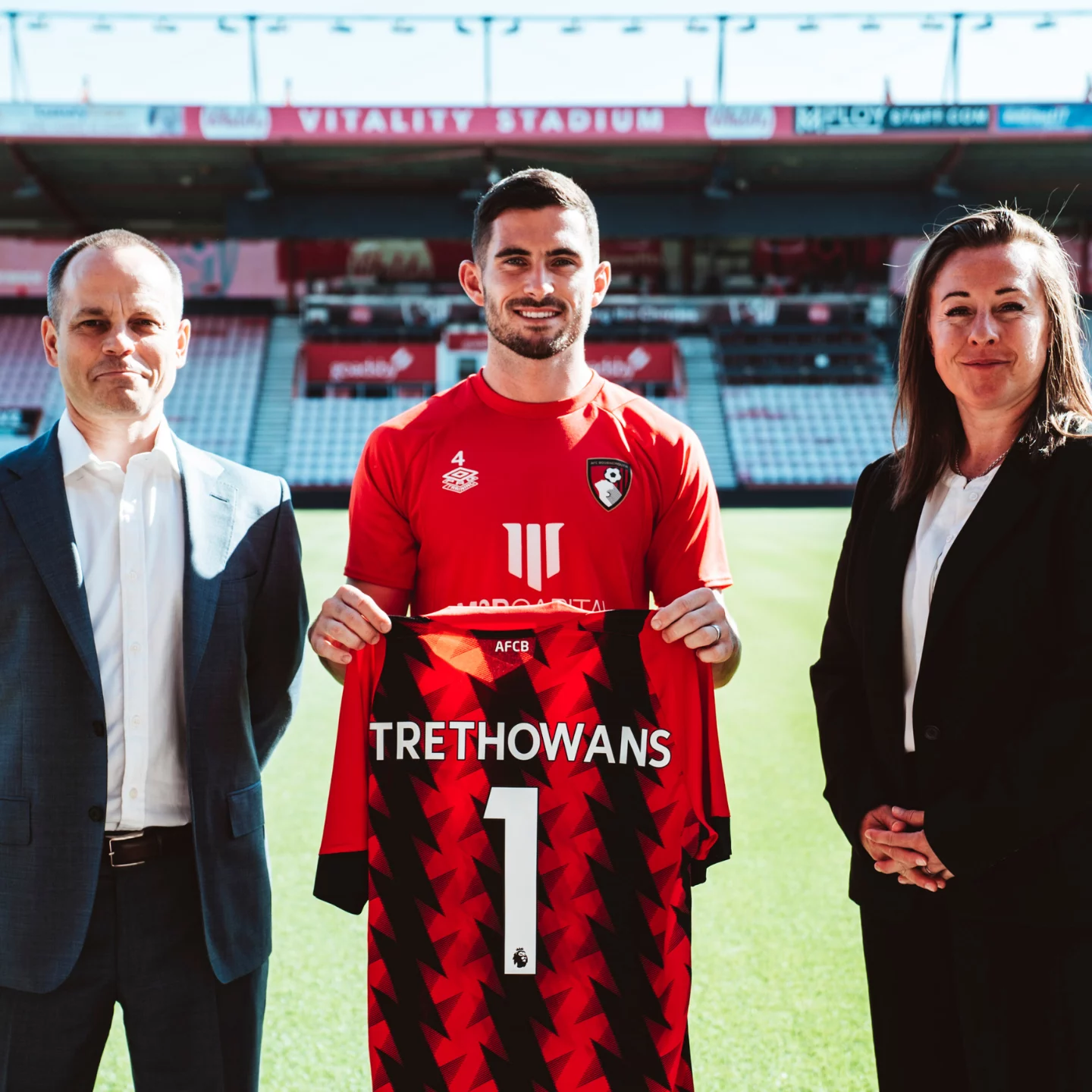 Mike Watson and Kathryn Evans standing with football player holding Trethowans AFCB football shirt