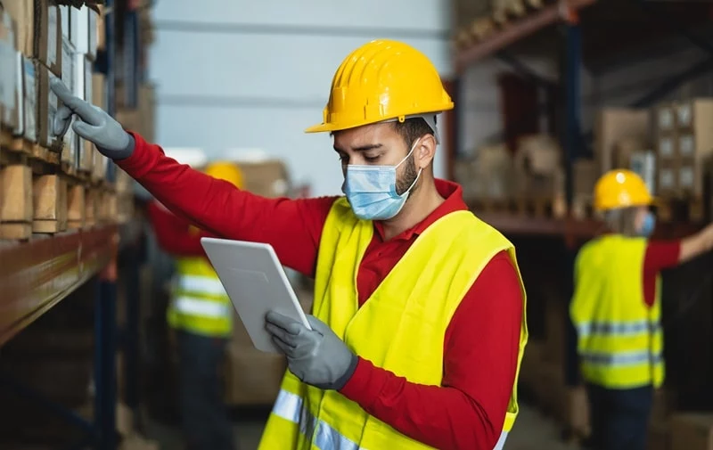 man with covid mask on and looking at tablet and stock in warehouse