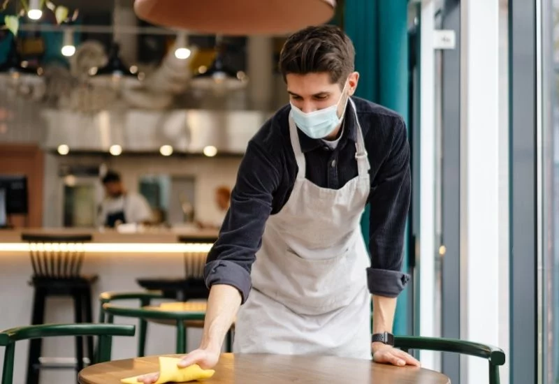 man with mask wiping a table