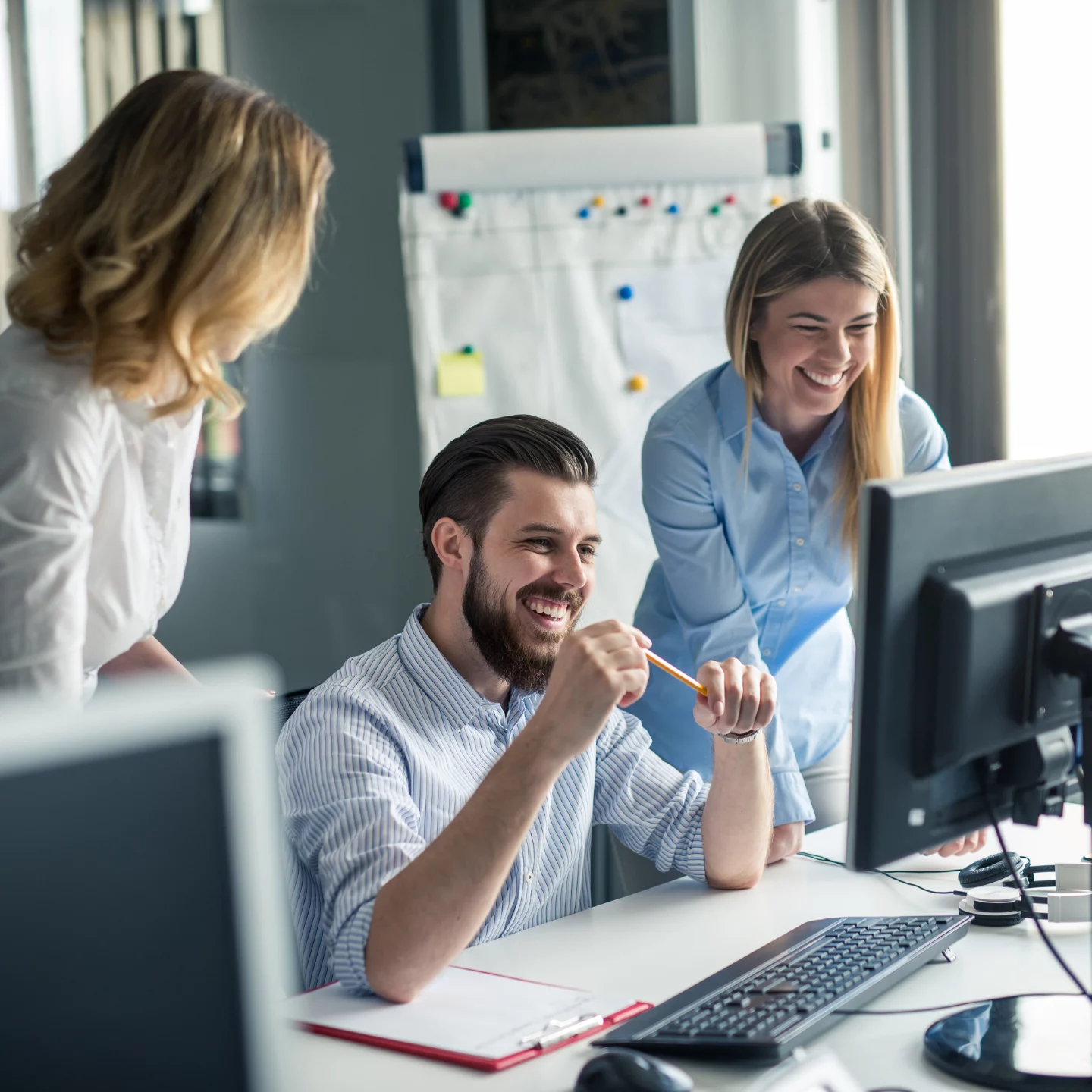 3 colleagues sitting/ standing around monitor and laughing