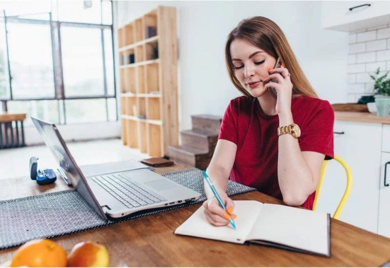 Women writing on note book infront of laptop