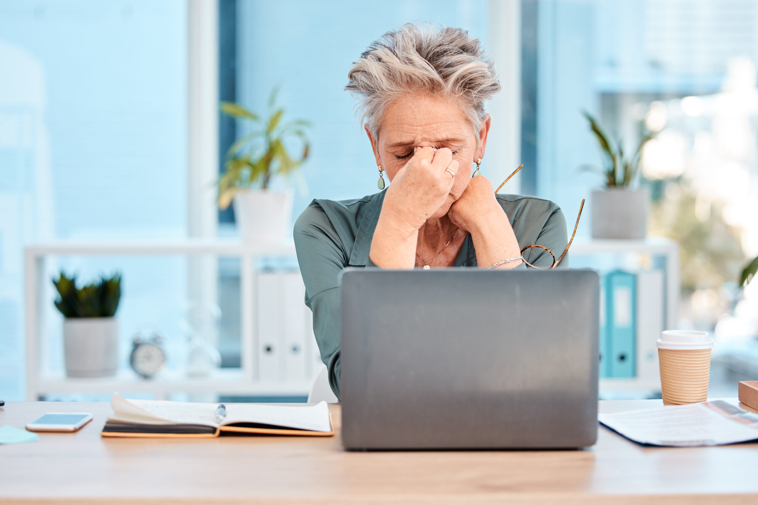 woman with laptop, holding her forehead in stress