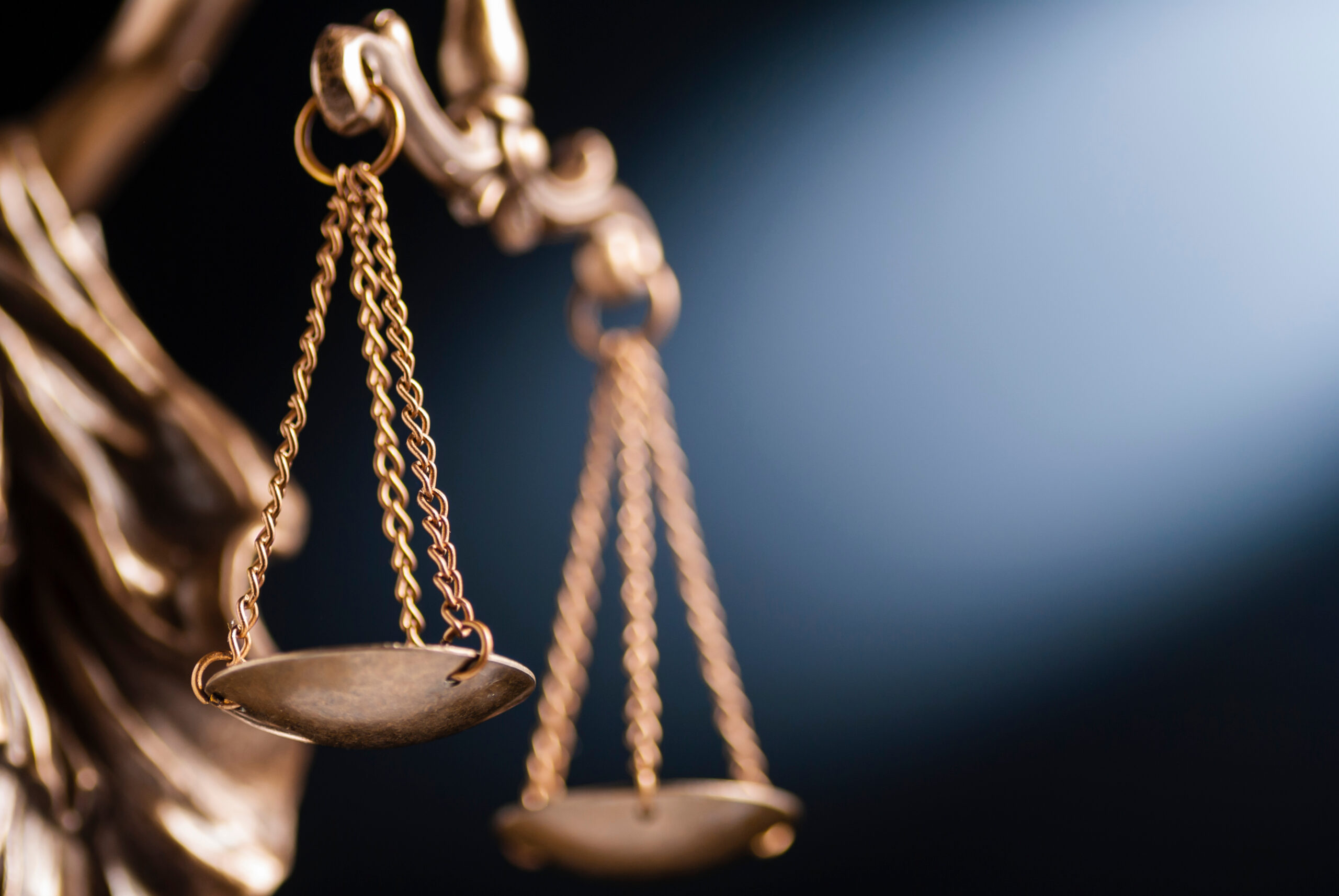 Close up on the scales of justice on a small bronze statue over a blue background