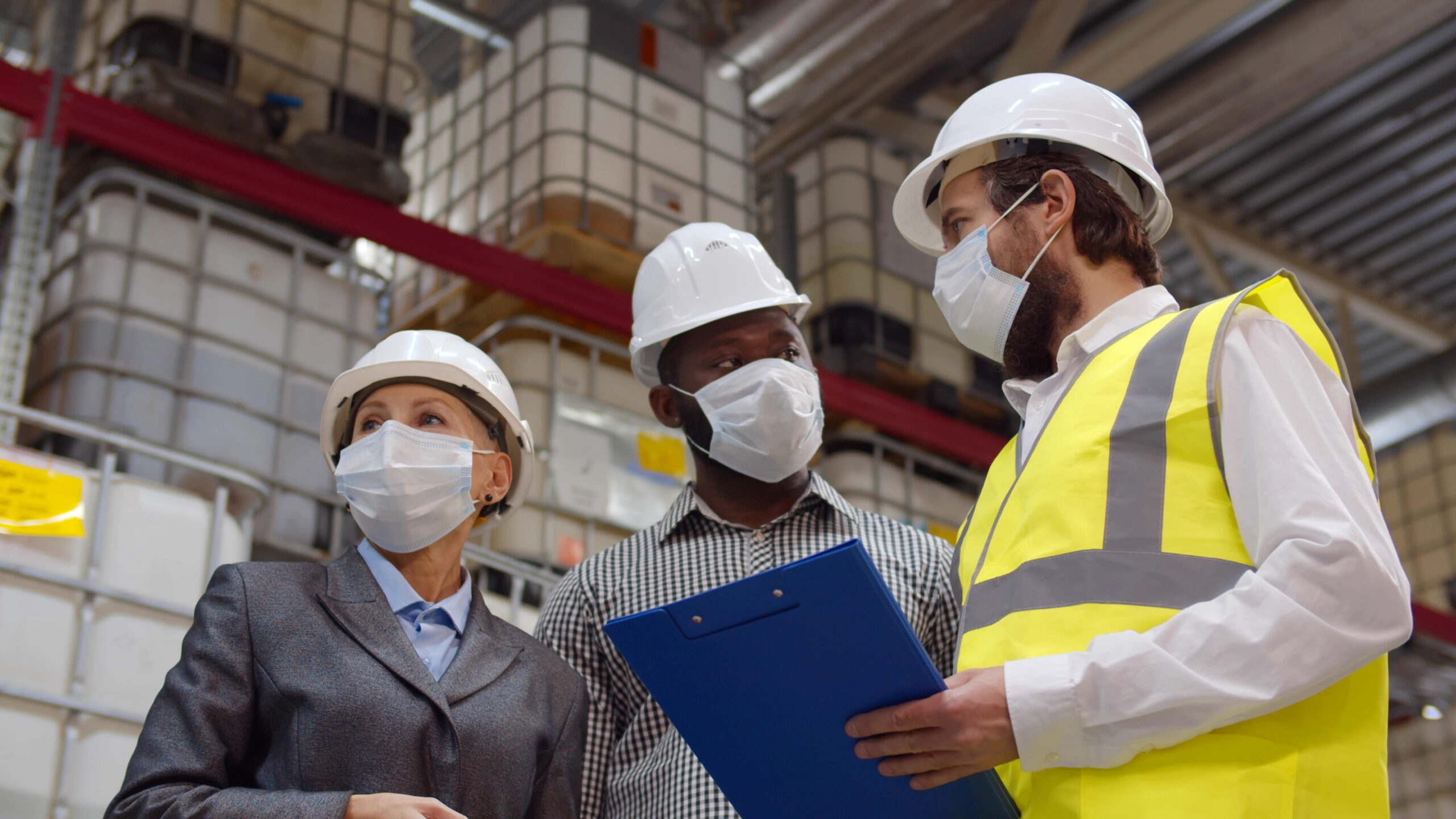 three health and safety inspector in warehouse with hard hats and masks on