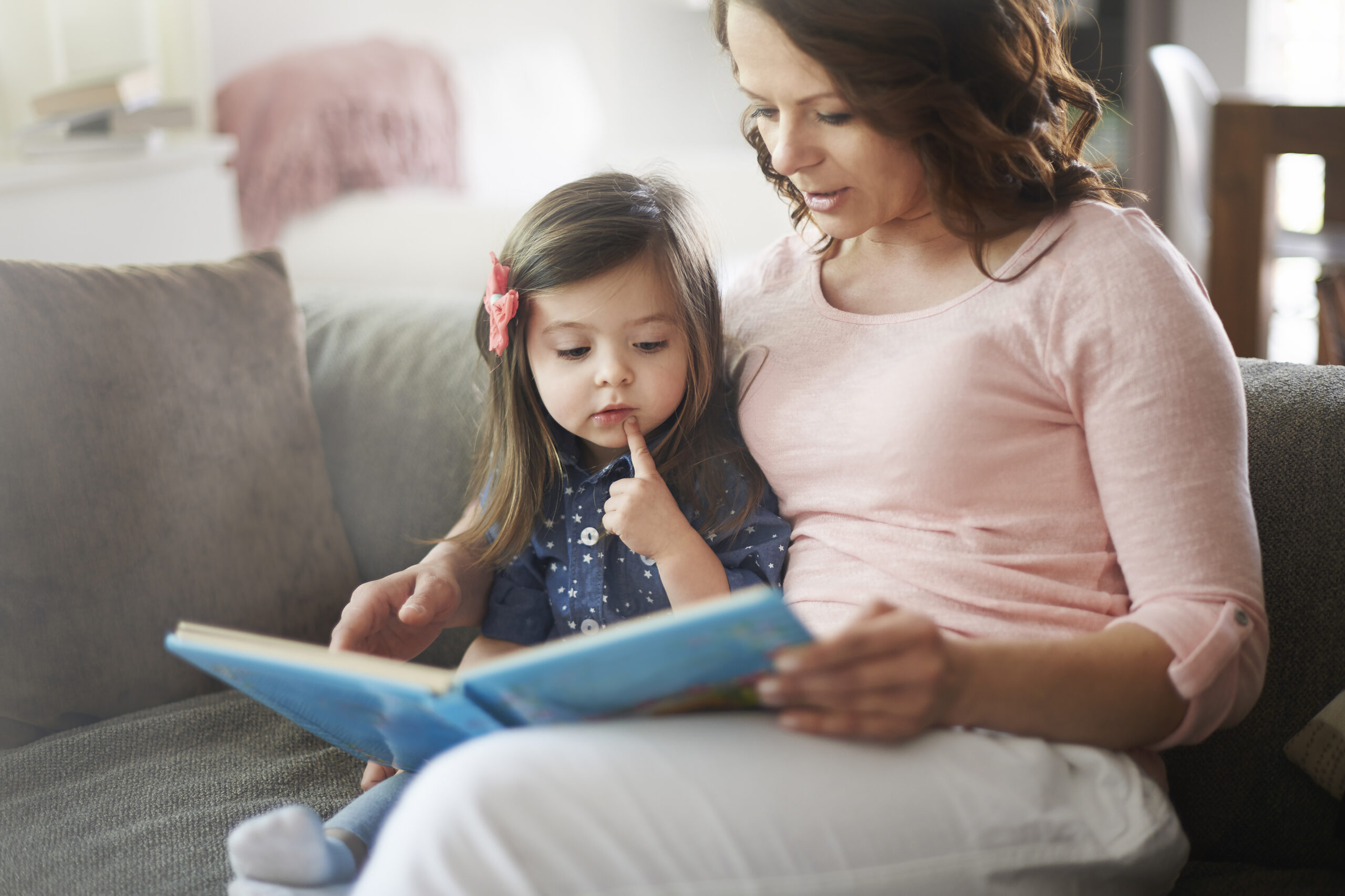 Mum reading a book to her daughter on the sofa