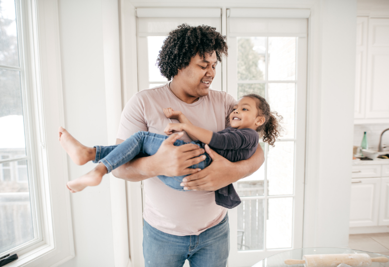 father playing and holding daughter in house