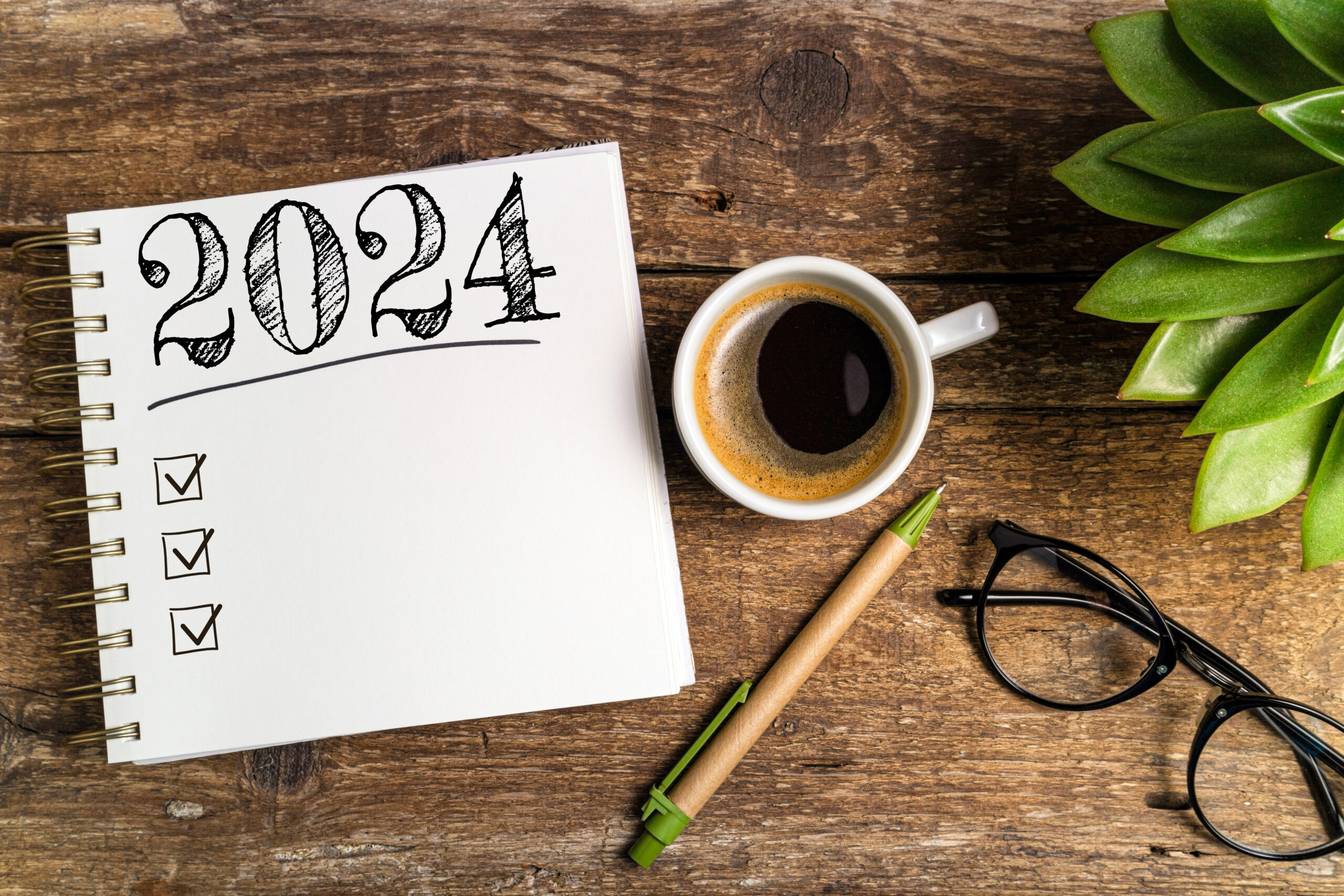 New year goals 2024 on desk. 2024 goals list with notebook, coffee cup, plant on wooden table. Resolutions, plan, goals, action, checklist, idea concept