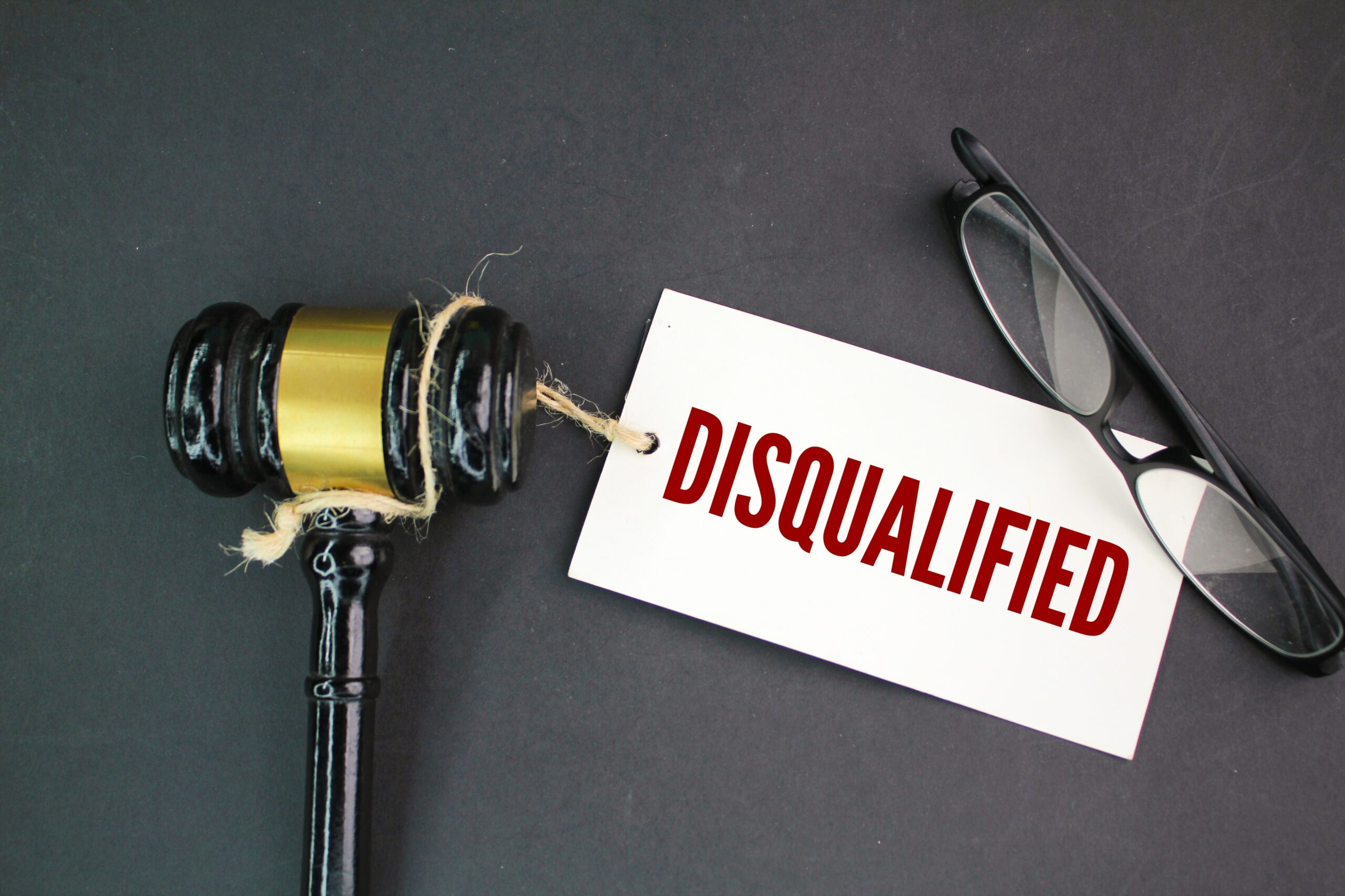 judge's gavel, glasses and a paper tag with the word disqualified. concept of disqualification